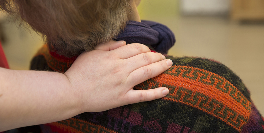 Person i rullstol med en underssköterskas hand på axeln.