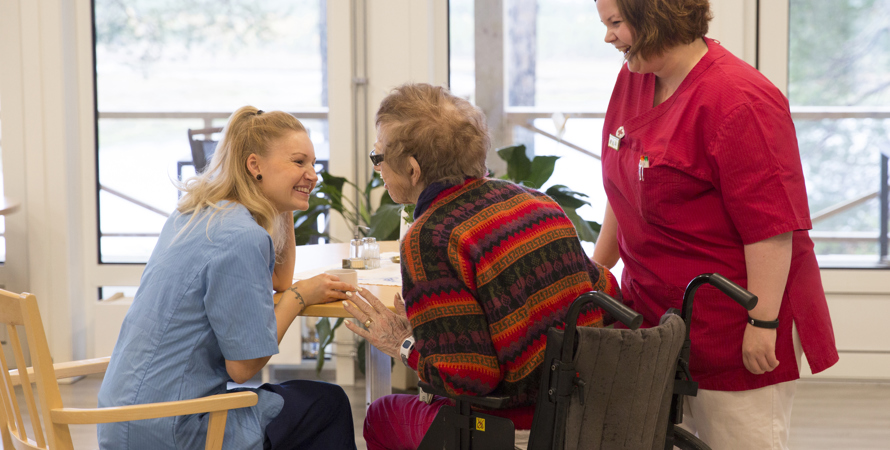 Två glada undersköterskor och en brukare i rullstol.
