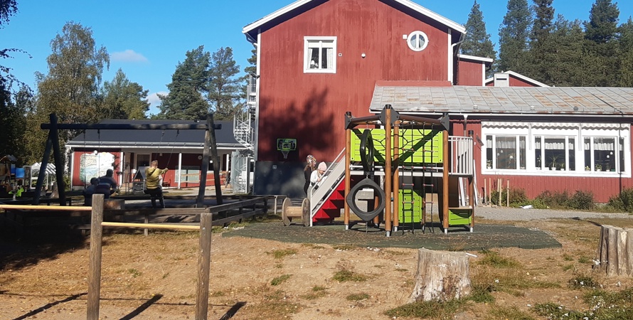 Rött stort hus med barn som leker på en lekplats