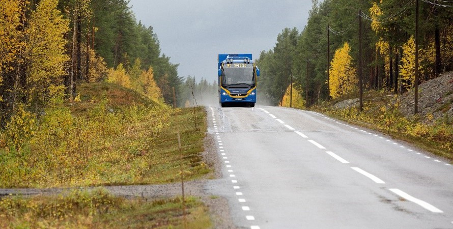 En buss på väg hitåt kör längs en väg i höstlandskap.