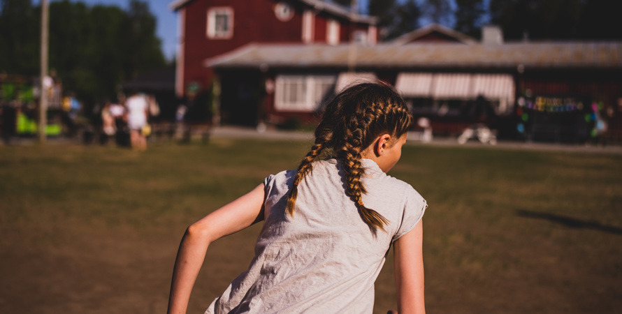 Ett barn med flätor springer mot en röd skolbyggnad.