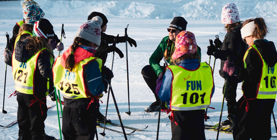 Barn  med skidutrustning och startnummerlapp som lyssnar på tränare