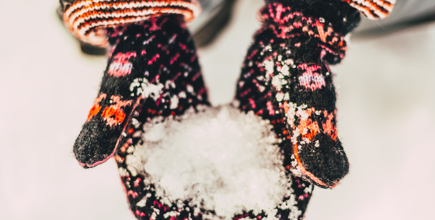 två öppna händer med stickade vantar på som håller i snö