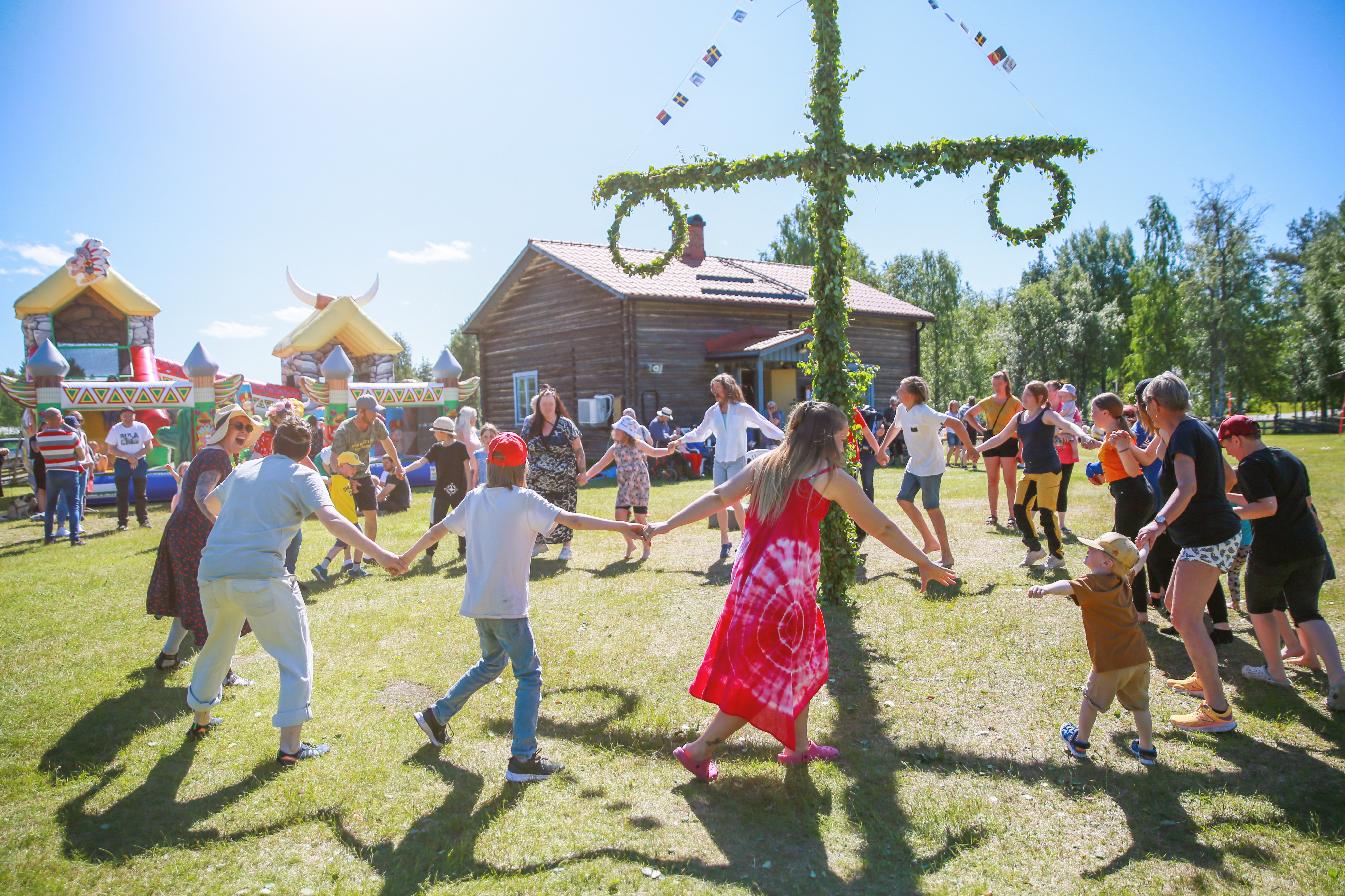 Barn och vuxna som dansar runt midsommarstång